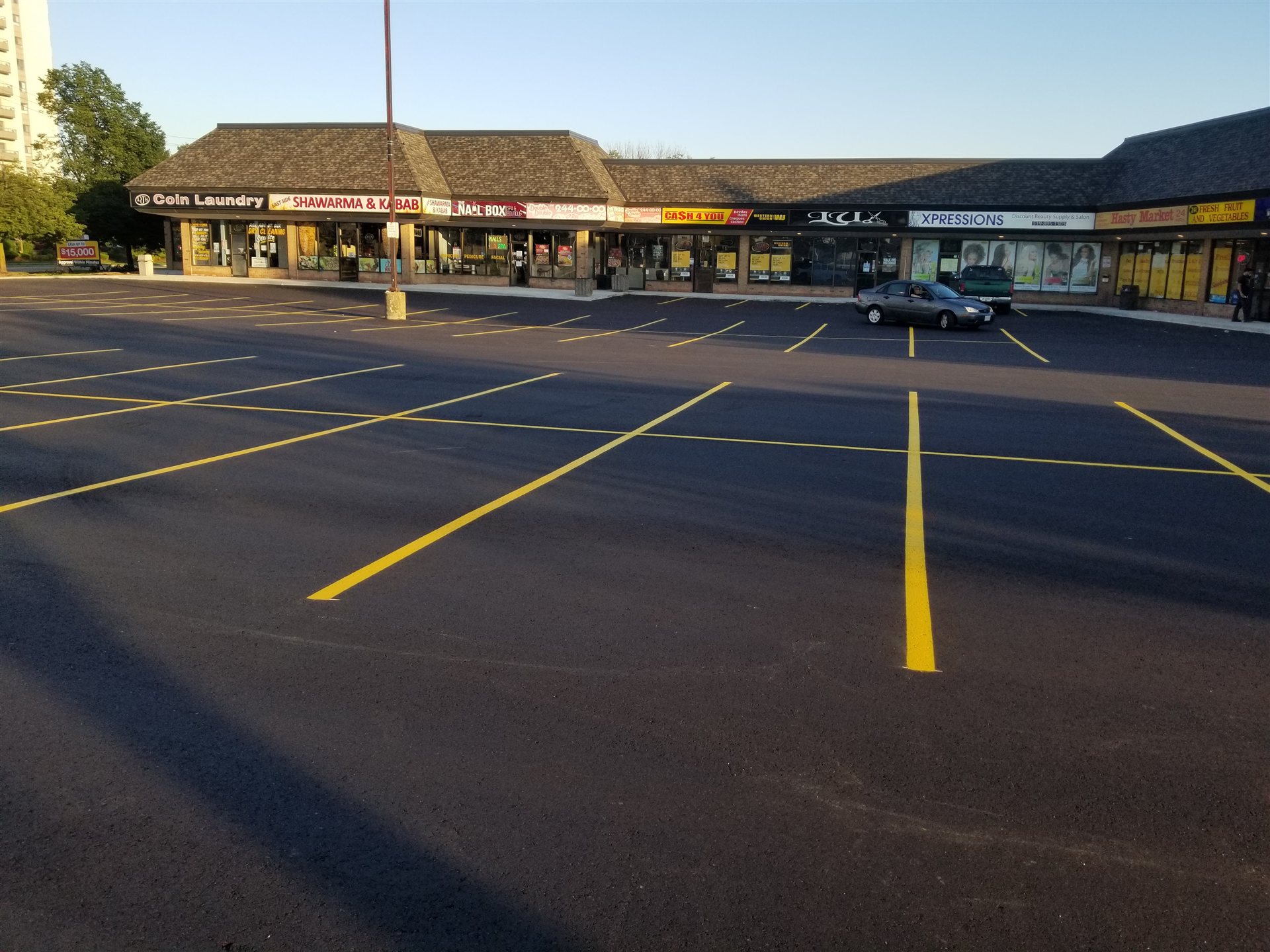 Asphalt parking lot with yellow parking-space markings in front of retail storefronts.