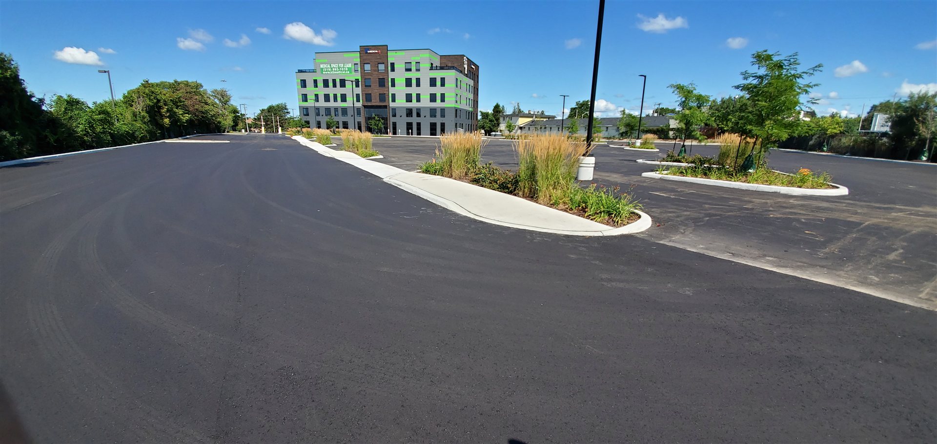 Wide asphalt parking area around curved concrete islands planted with grasses and trees.