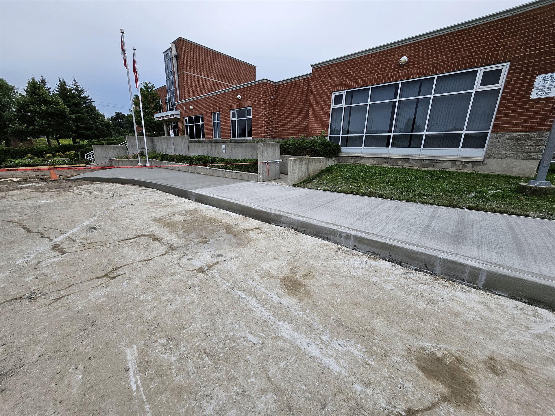 Concrete sidewalk and raised curb running along a brick building.