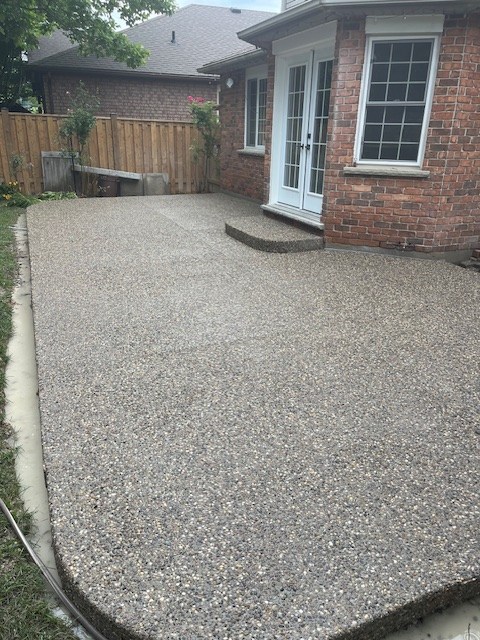 Exposed aggregate concrete patio with a curved edge and step at a brick house